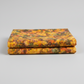 Expressions Batiks Hand-Dyed Orange Multi I quilting cotton fabric by Riley Blake Designs – 2 neatly folded yards stacked on light grey background showing complex multicolor hand-dyed batik with golden amber-orange, olive green, slate blue-grey, and red-orange palette