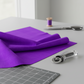 Interwoven Plum by Jason Yenter – quilt room lifestyle shot with folded fabric, cutting mat corner, spool of thread, scissors, and rotary cutter on light grey base