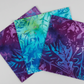 Tonga Batik Dreamer by Timeless Treasures – Pinterest close-up of three 5" charm squares fanned on light grey background showing vivid purple, teal, and blue-violet hand-dyed batik patterns with tropical leaf wax resist motifs