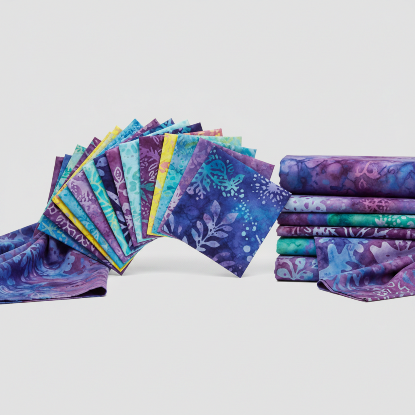 Tonga Batik Dreamer by Timeless Treasures – charm pack squares fanned alongside coordinating folded yardage cuts on light grey background, showing collection palette of deep purples, teals, aquas, and blue batiks