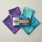 Tonga Batik Dreamer by Timeless Treasures – Tonga Treats charm pack with two coordinating fat quarters in soft purple and bright teal batik fanned on cream linen surface showing collection palette