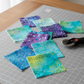 Tonga Batik Dreamer by Timeless Treasures – charm pack squares arranged on grey cutting mat on wood table with rotary cutter, showing purple, teal, aqua, and chartreuse batik fabrics ready for quilting