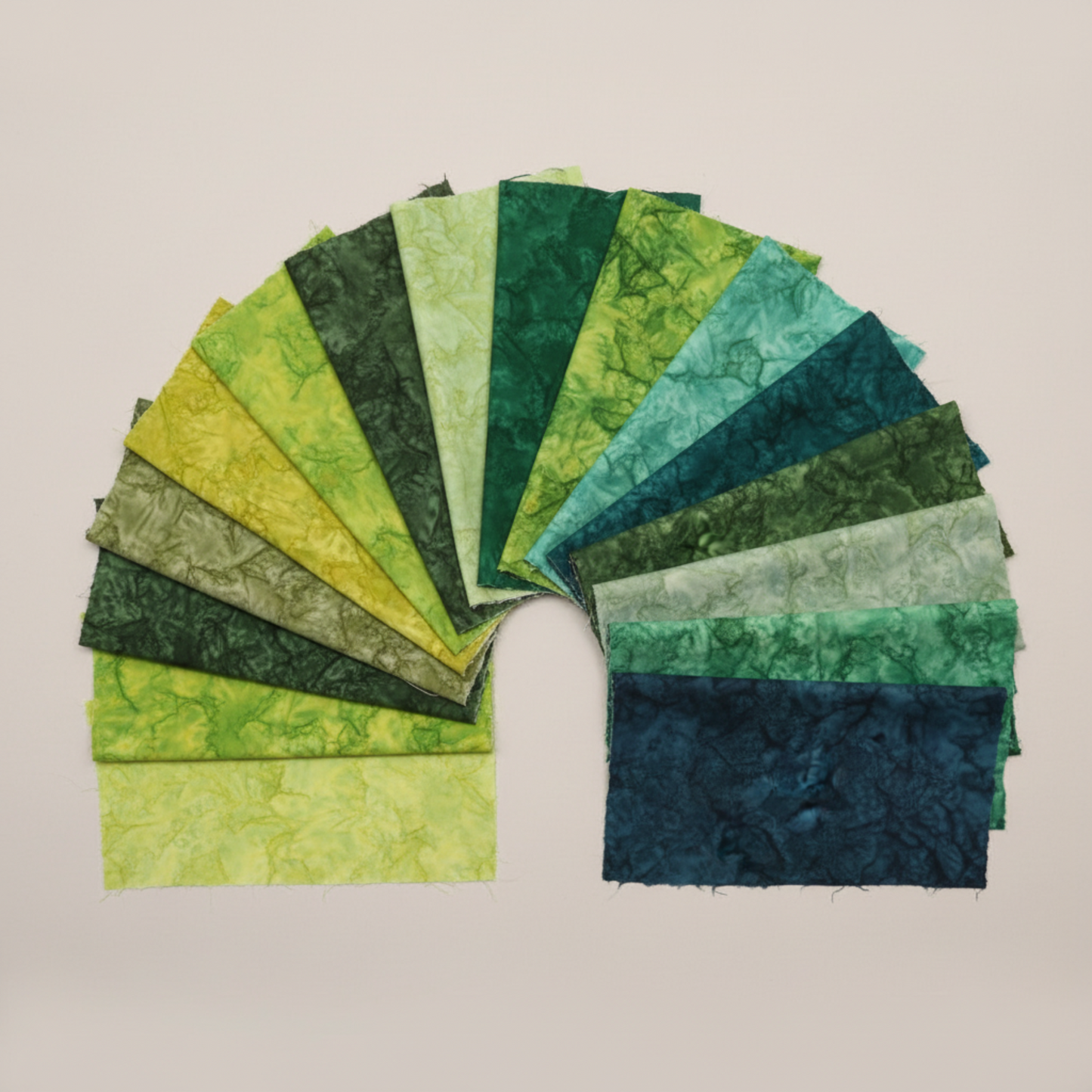 Artisan Batiks Prisma Dyes Rainforest by Robert Kaufman – 40 pre-cut 2.5" strips fanned in wide arc on light grey background showing full color progression from yellow-green and chartreuse through olive, forest green, emerald, teal, aqua, and deep navy-teal batik