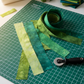 Artisan Batiks Prisma Dyes Rainforest by Robert Kaufman – Pinterest workspace shot showing 2.5" batik strips laid on green cutting mat with rotary cutter, coiled strip roll, coordinating fat quarter stack, and sewing machine in quilting studio setting