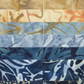 Tonga Batik Moonlit by Timeless Treasures – close-up grid of 2.5" strips showing batik wax resist texture and pattern detail, progressing from cream and warm sand through golden taupe, slate blue, periwinkle, denim, and deep navy with tropical leaf and botanical motifs