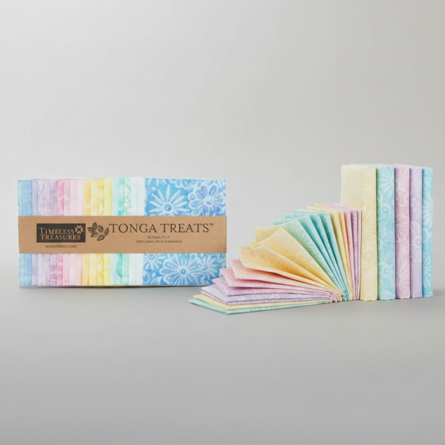 Tonga Batik Pixie by Timeless Treasures – Tonga Treats charm pack package alongside 42 pre-cut 5" squares mini-fanned and standing upright on light grey background, showing soft pastel rainbow palette of lavender, blush pink, yellow, mint, and sky blue hand-dyed batik