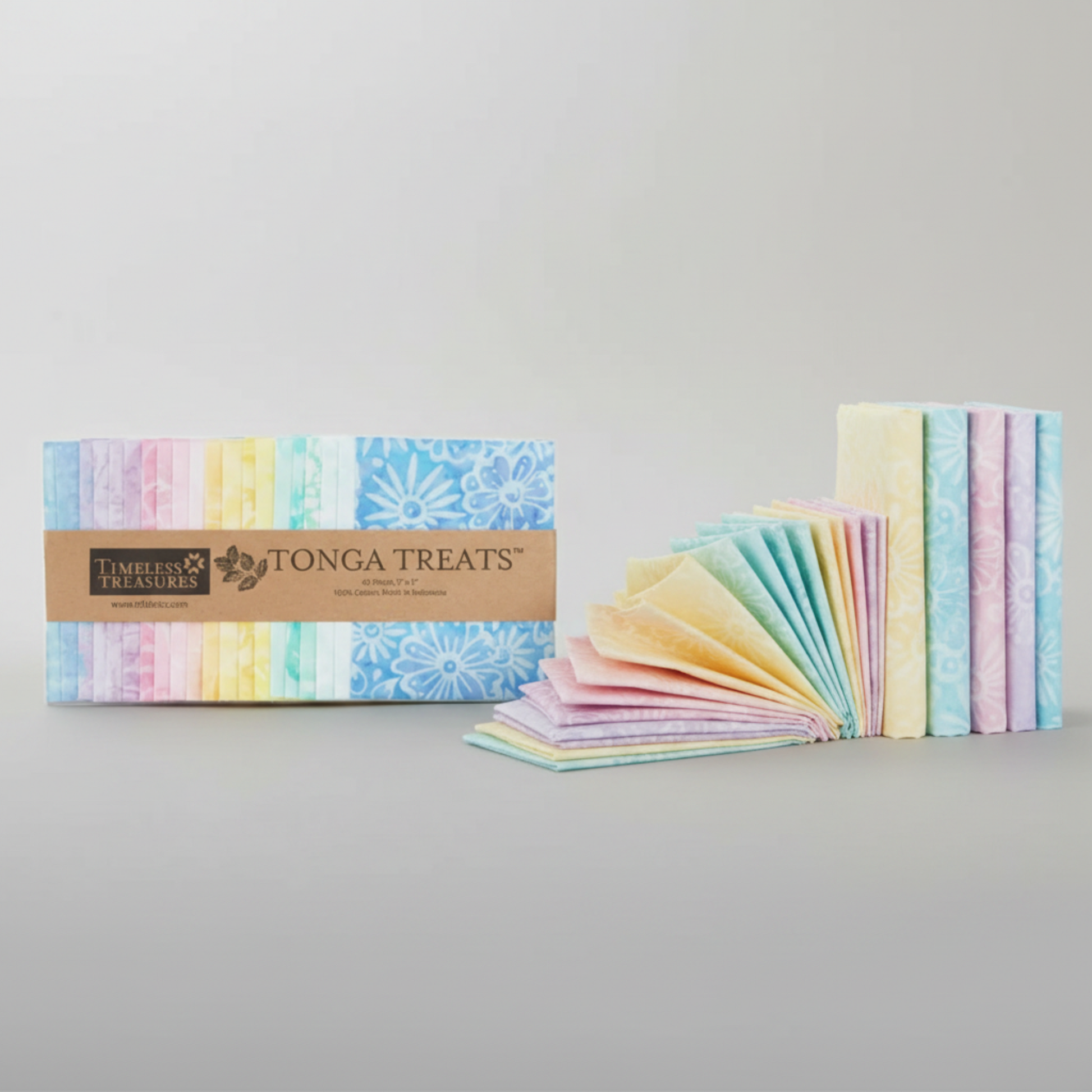 Tonga Batik Pixie by Timeless Treasures – Tonga Treats charm pack package alongside 42 pre-cut 5" squares mini-fanned and standing upright on light grey background, showing soft pastel rainbow palette of lavender, blush pink, yellow, mint, and sky blue hand-dyed batik