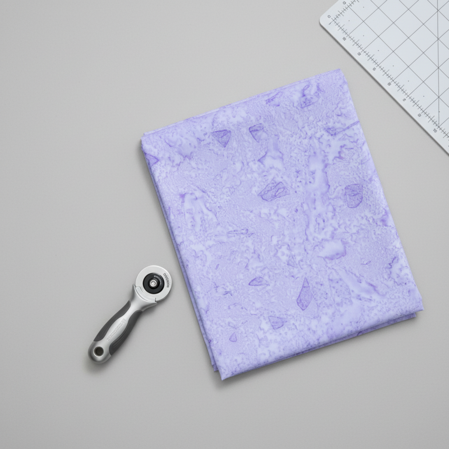 Expressions Batiks Hand-Dyed Periwinkle by Riley Blake Designs – lifestyle shot with folded fabric, rotary cutter and cutting mat, clean minimal setting