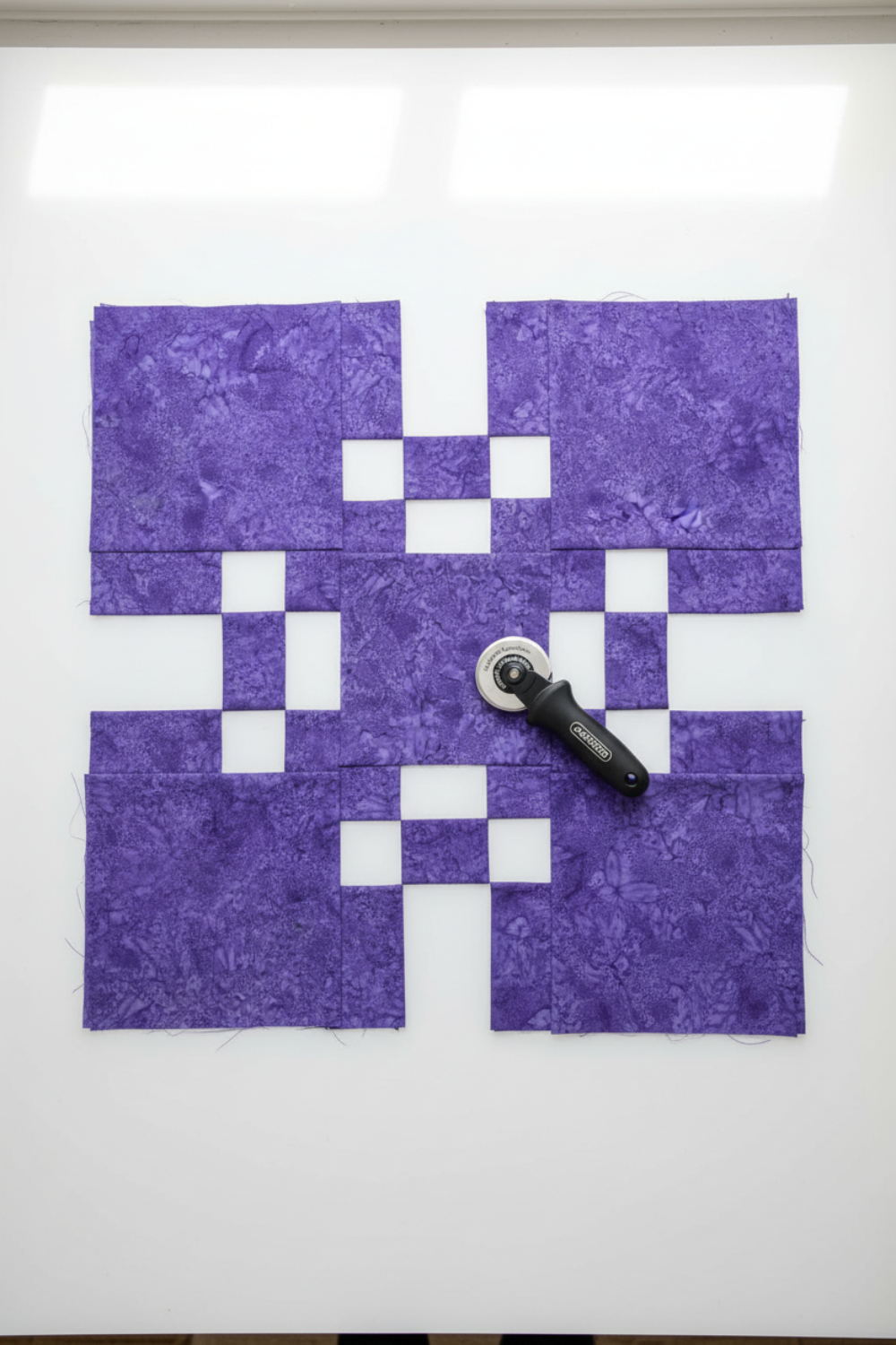 Expressions Batiks Hand-Dyed Purple II – fabric cut in strips and squares for quilt project, rotary cutter visible