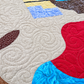 Close-up of Starry Night quilt showing spiral quilting across the light patterned background and red and turquoise camel saddle.