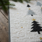 Handmade winter quilt laid flat on a rustic wood table, styled with evergreen branches and candles, highlighting modern tree design and swirling quilting.