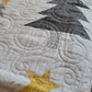 Close-up of handmade quilt showing gray tree motif, gold star appliqué, and swirling free-motion quilting on a soft white background.