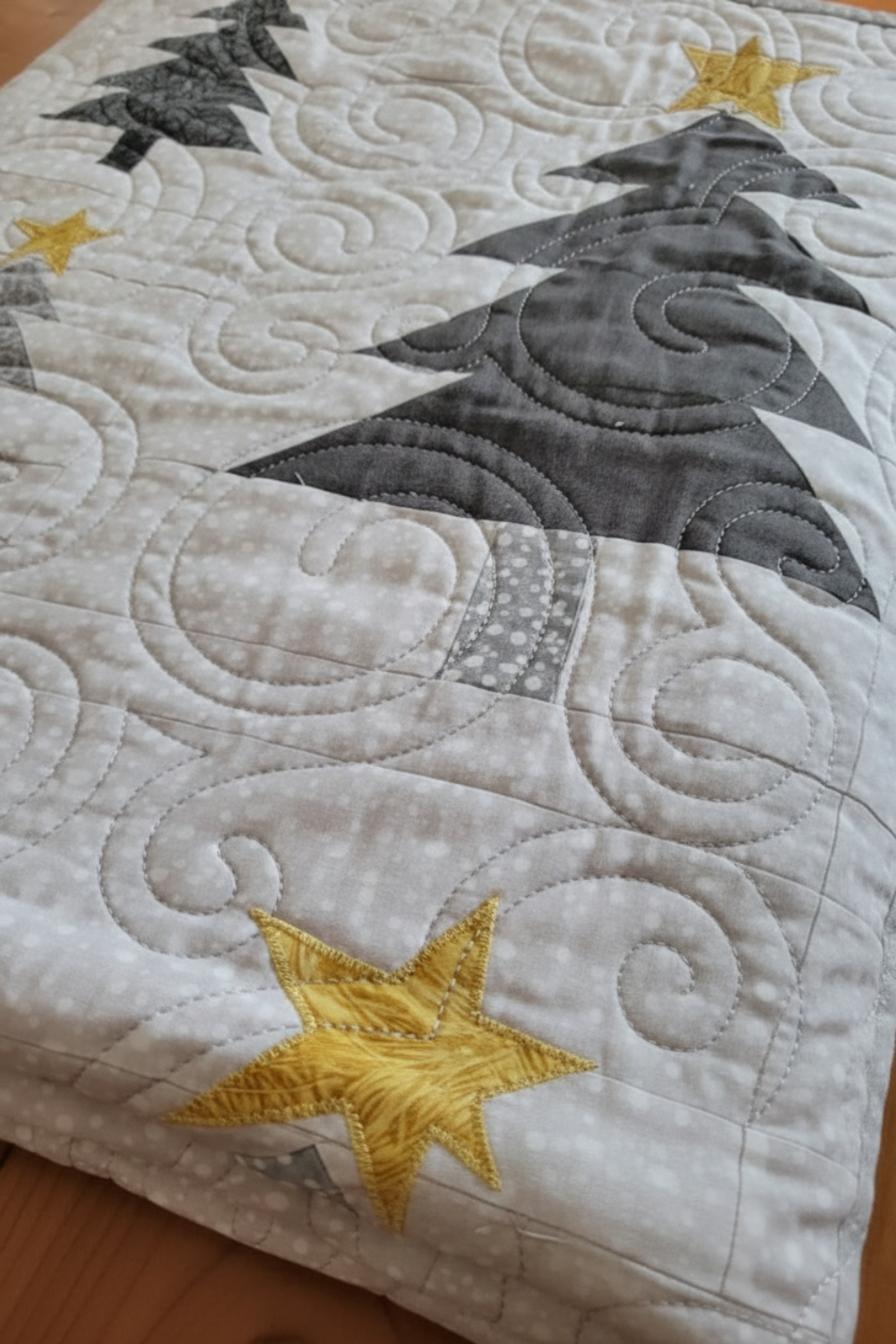 Close-up of handmade quilt showing gray tree motif, gold star appliqué, and swirling free-motion quilting on a soft white background.
