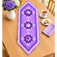 Purple Twilight quilted table runner on a wood dining table beside purple and white hydrangeas, a floral teacup, cookies and a lavender napkin.