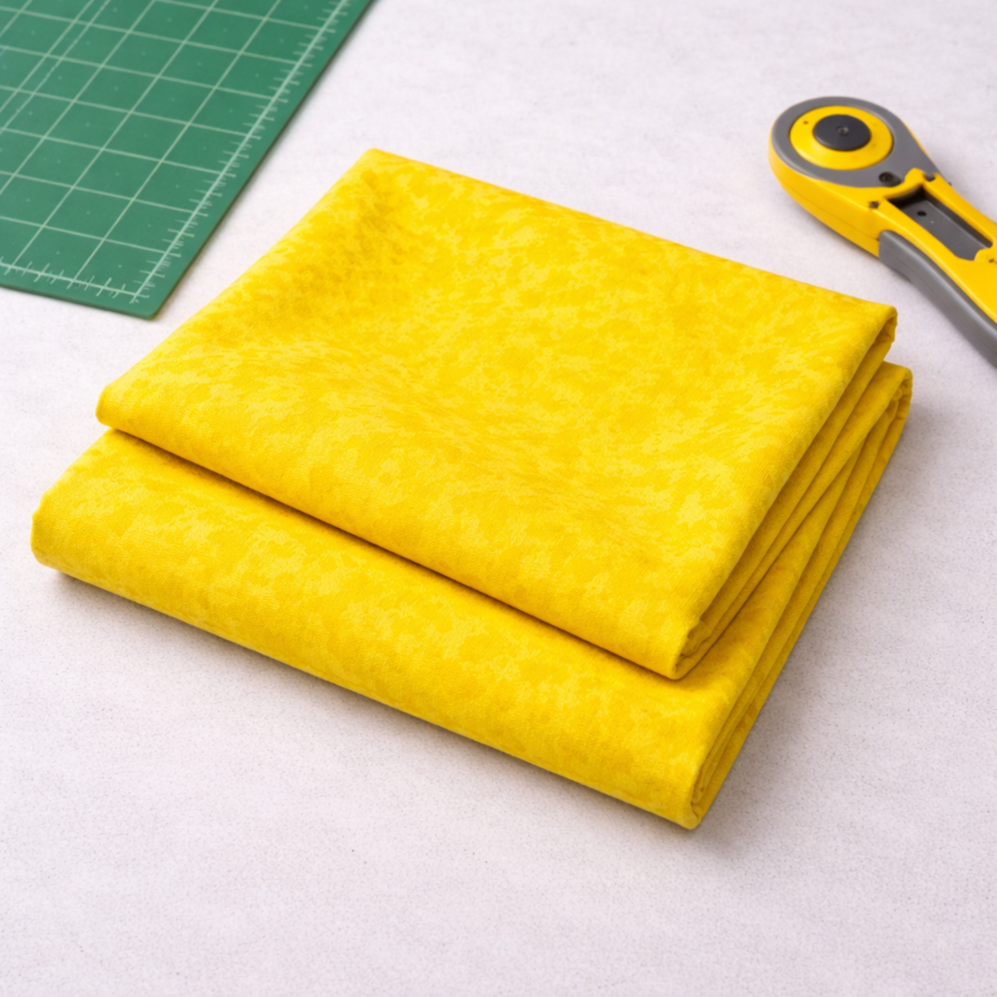 Expressions Batiks Hand-Dyed Bumblebee quilting cotton fabric by Riley Blake Designs – bright sunny yellow batik ready for quilting project with rotary cutter and edge of cutting mat visible on light grey background
