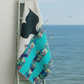 Colorful quilt with geometric patterns draped over a ladder by the ocean with seagulls.