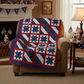 Star-patterned red, white, and blue quilt draped over a beige armchair in a room with American flag decorations.