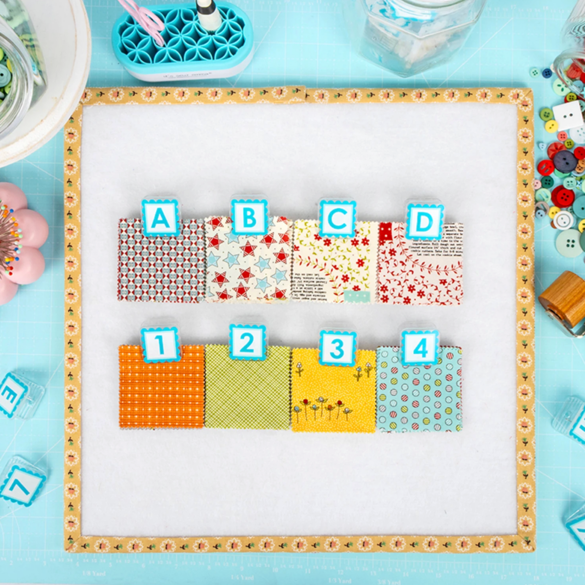 AlphaClippies quilt labeling clips arranged on fabric squares with alphabet and number markers on quilting design board
