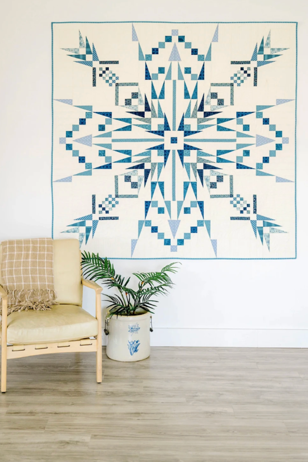 Blue and white Northern Lights quilt hanging on wall in modern room with chair and potted plant