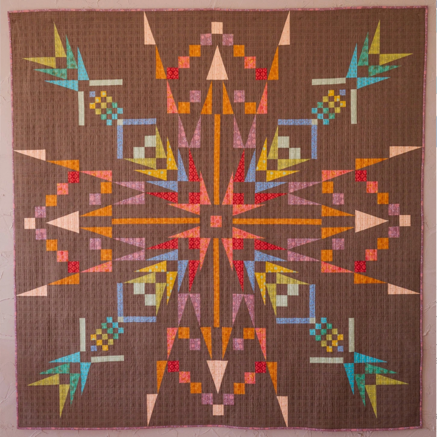 Close-up of Northern Lights quilt featuring vibrant geometric starburst pattern in pink, orange, teal, yellow, and brown fabrics