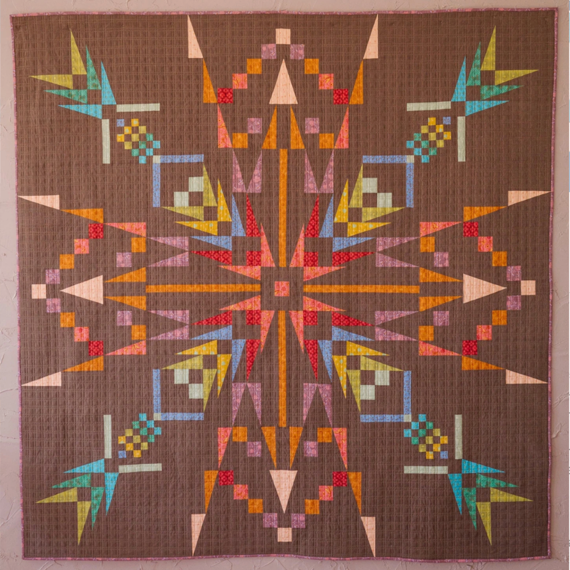 Close-up of Northern Lights quilt featuring vibrant geometric starburst pattern in pink, orange, teal, yellow, and brown fabrics