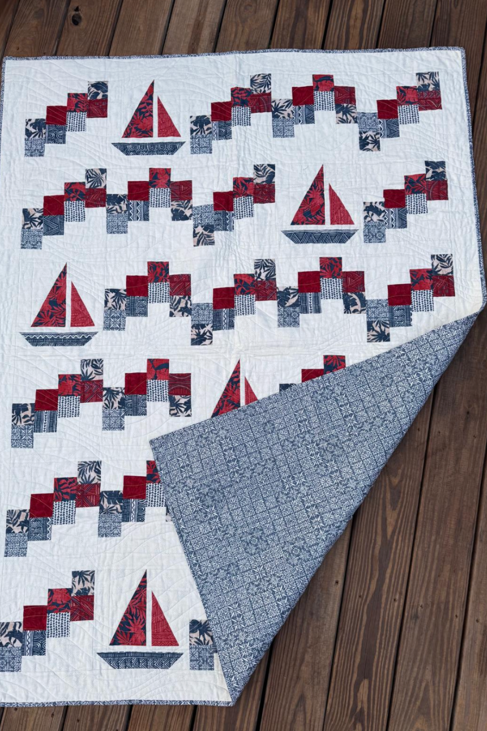 Handmade Sailing School sailboat quilt displayed on a wooden deck with one corner folded back to show the blue patterned backing.