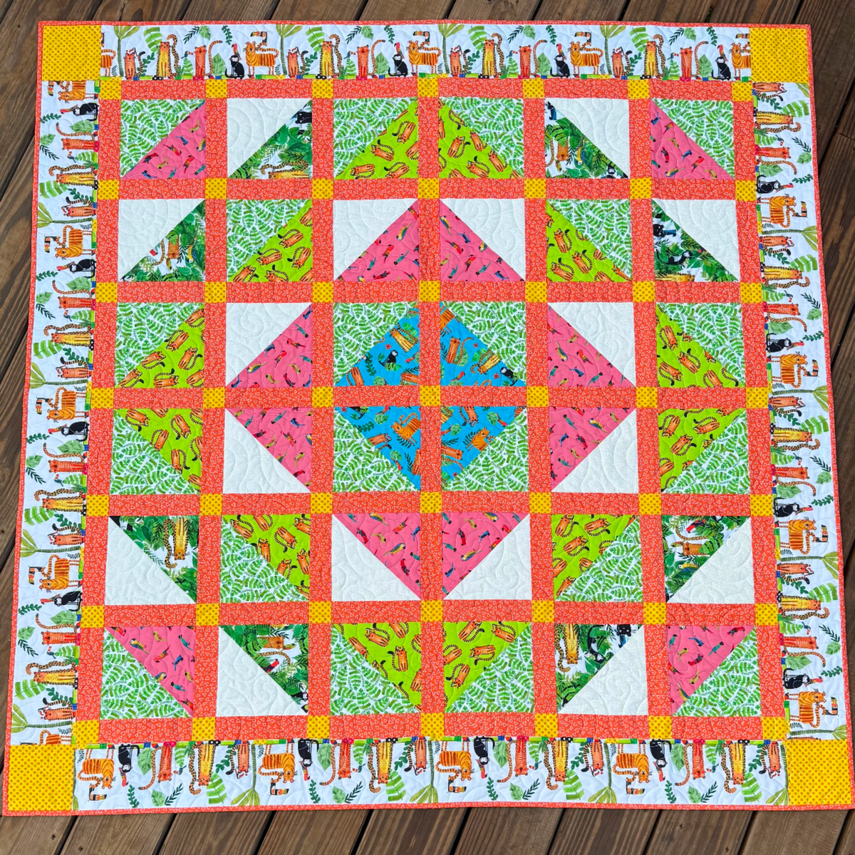 Handmade In the Jungle quilt featuring colorful jungle animals, tropical prints, coral sashing, yellow accents, and animal-print border.
