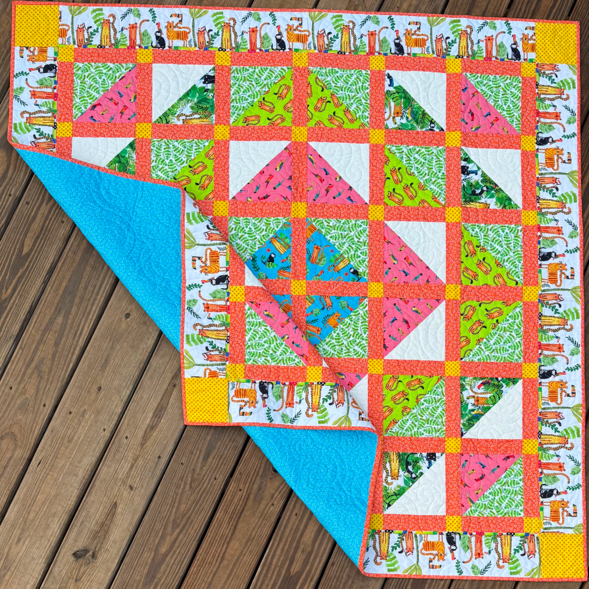 Handmade In the Jungle quilt folded back to show the bright turquoise backing and colorful jungle animal patchwork front.