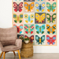 Colorful butterfly quilt hanging on a wall above a chair and small table.