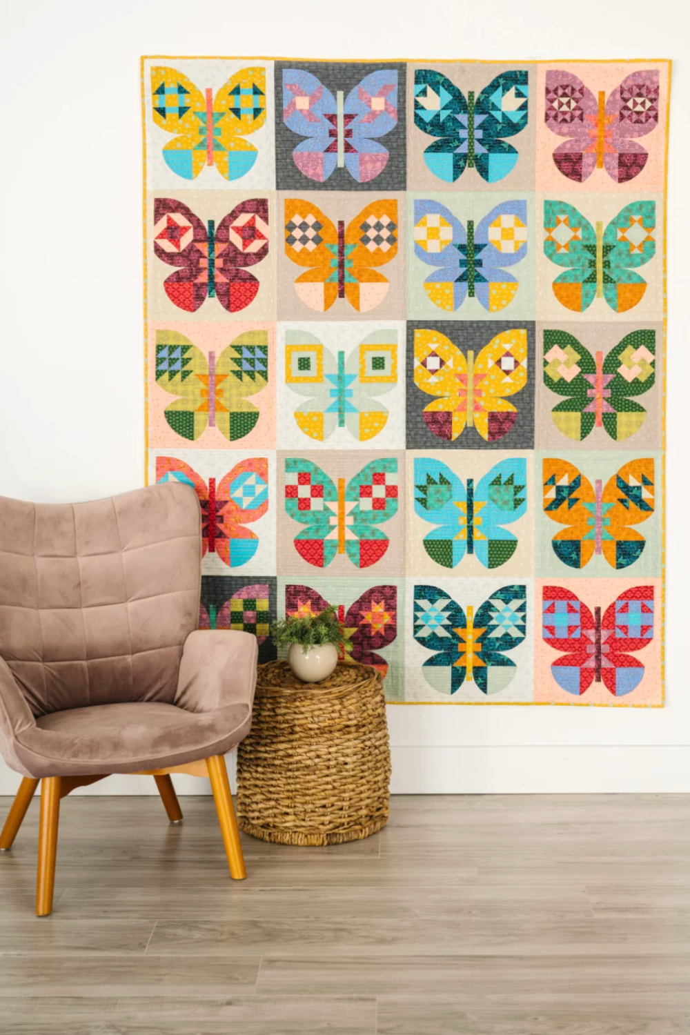 Colorful butterfly quilt hanging on a wall above a chair and small table.