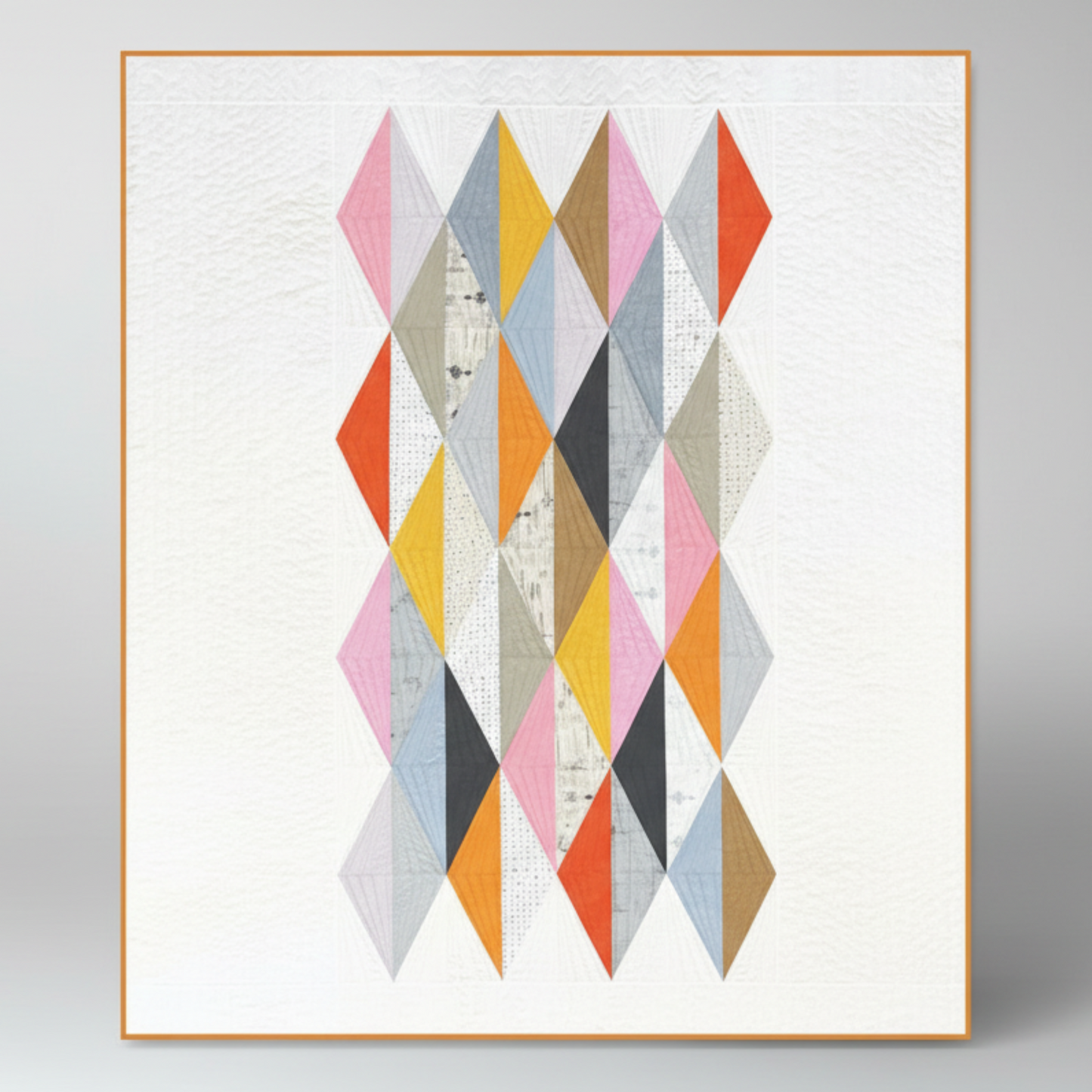 Framed geometric quilt with colorful diamond patterns on a white background