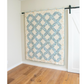 Quilt with geometric pattern hanging on a wall in a room with wooden flooring.