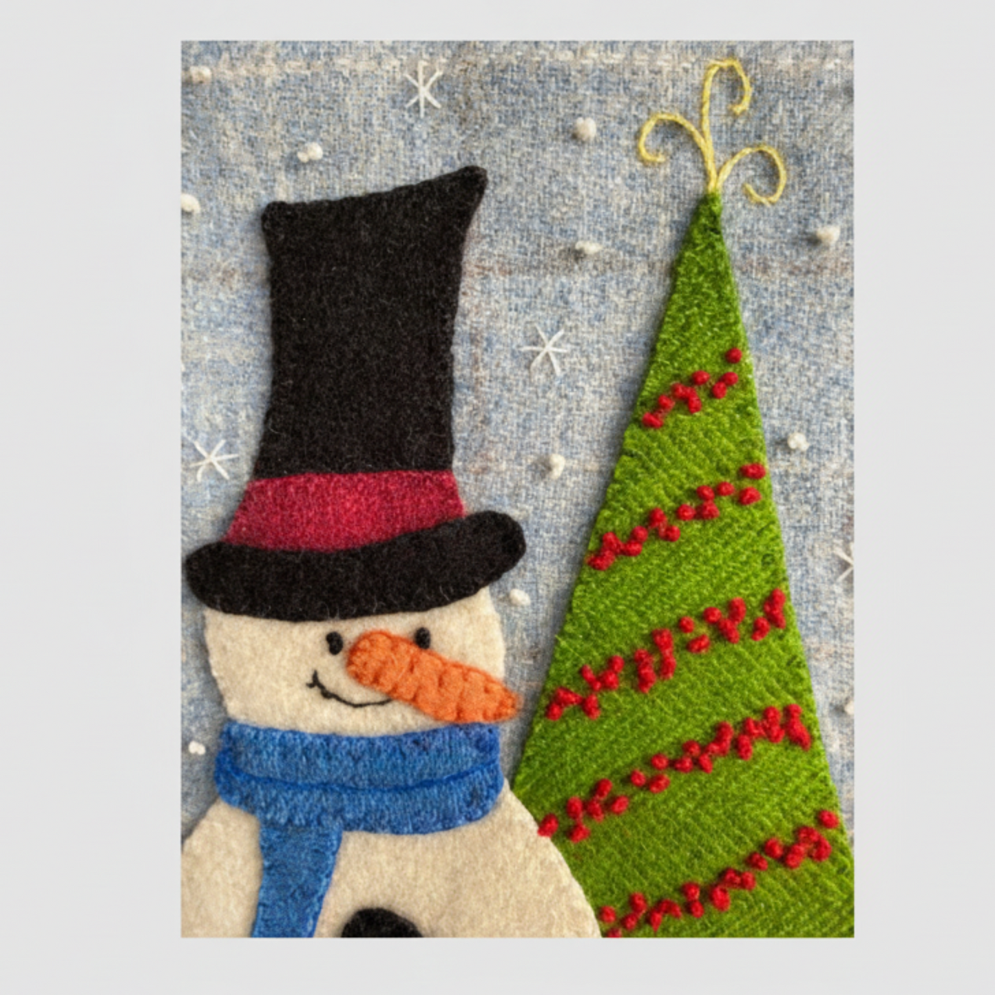 Felt snowman with a top hat and carrot nose next to a felt Christmas tree on a textured background.