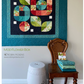 Colorful quilt titled 'Mod Flower Box' by Robin Pickens on a wall with a wooden chair and white stool below.