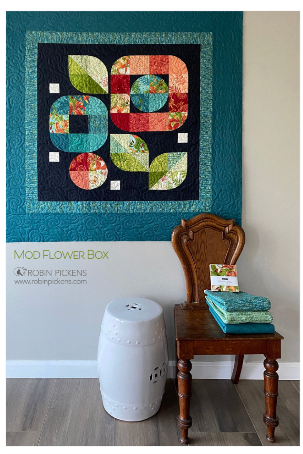 Colorful quilt titled 'Mod Flower Box' by Robin Pickens on a wall with a wooden chair and white stool below.