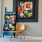 Colorful geometric quilt on a wall with a wooden chair below and a framed quilt in the background.