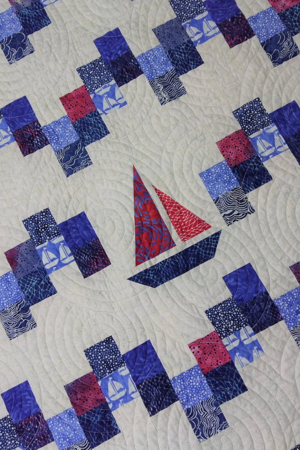 Quilt with sailboat pattern in blue and red on a white background