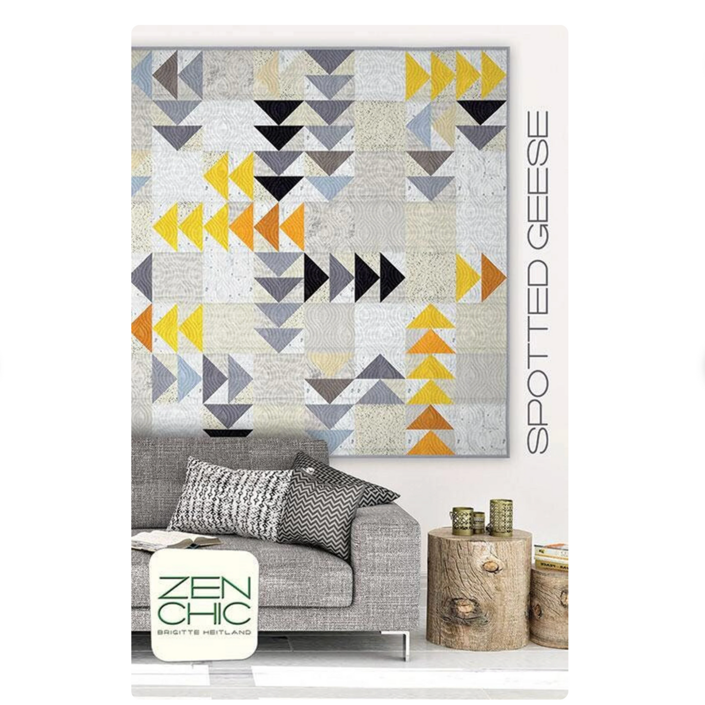 Geometric triangle patterned quilt on a white wall above a gray sofa with 'Spotted Geese' branding.
