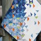 Quilt with geometric pattern draped over a wooden post by water
