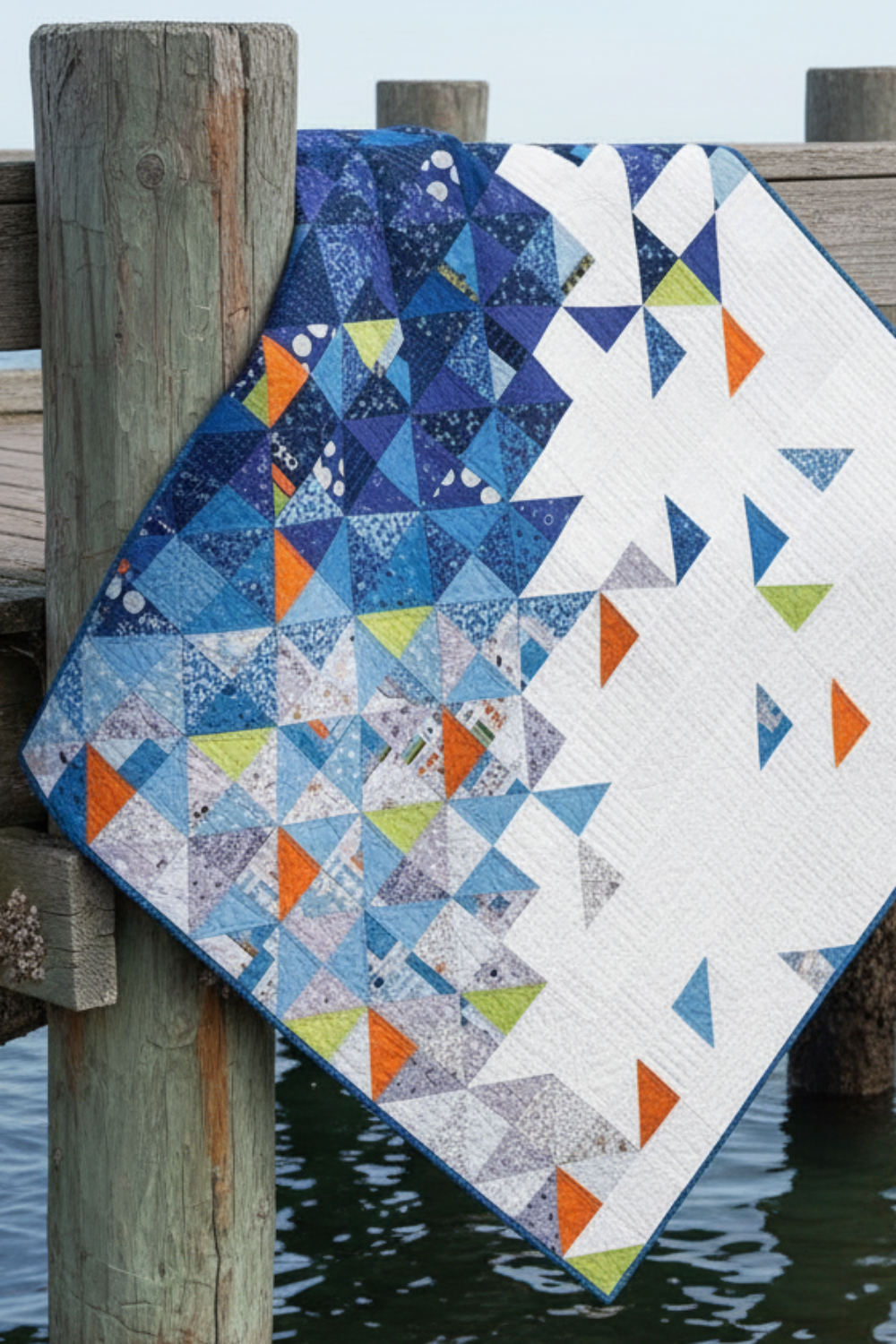 Quilt with geometric pattern draped over a wooden post by water