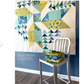 Quilt with geometric pattern on a wall above a white chair with folded fabric.
