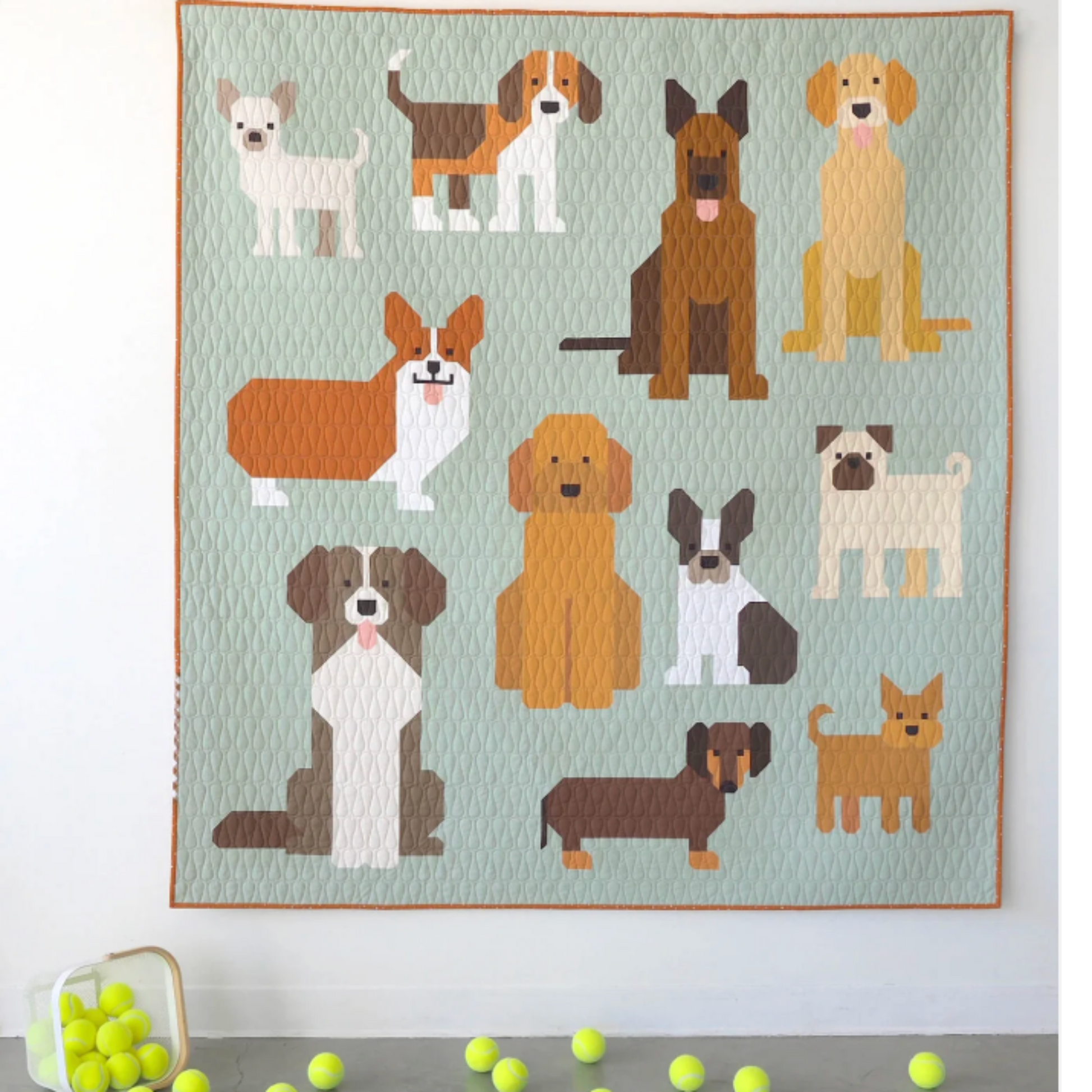 Quilt with illustrations of various dogs on a light blue background, with tennis balls on the floor.