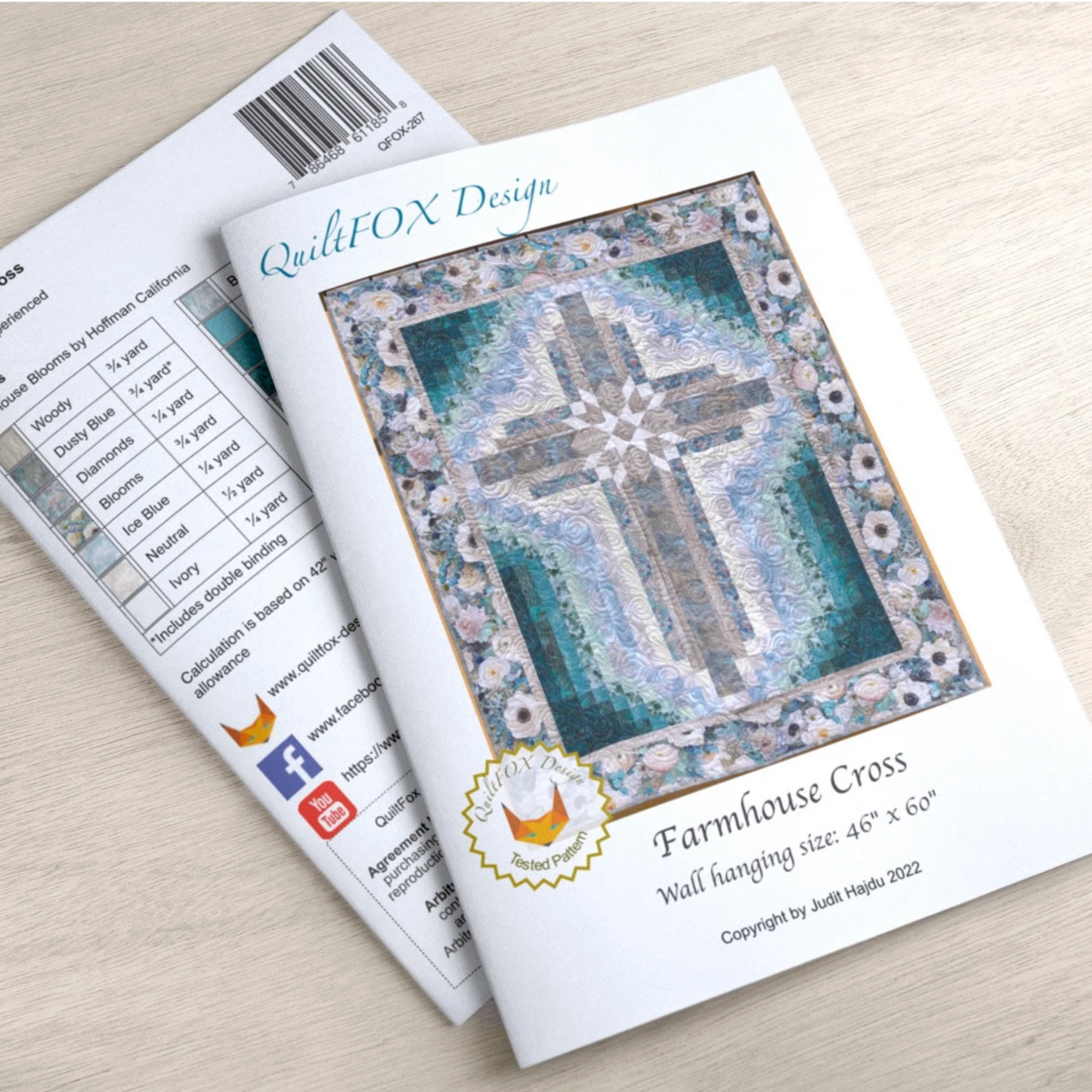 Quilt pattern book titled 'Farmhouse Cross' by QuiltFOX Design on a light wooden surface.