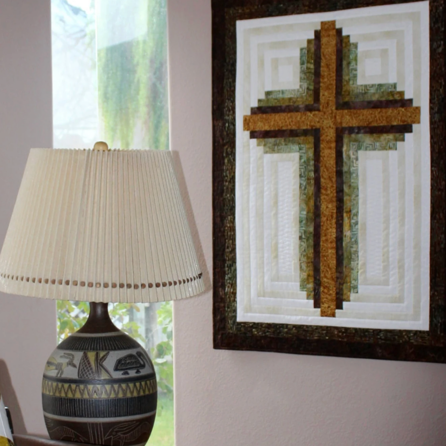 Decorative cross artwork on a wall next to a lamp with a white shade.