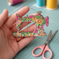 Close-up of Superbloom sewing machine needle minder held in hand, showing floral enamel details and magnetic needle holder