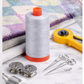 Aurifil Mako Cotton Thread 50wt Aluminum surrounded by rotary cutter, needles, and quilting tools.