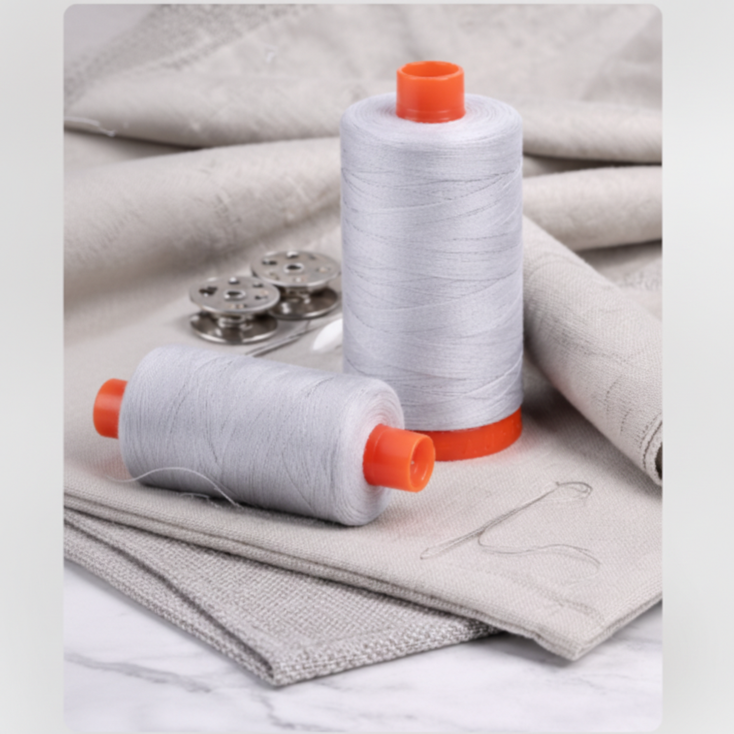 Aurifil 50wt Aluminum cotton thread spools with metal bobbins on neutral fabric, ideal for quilting and sewing.