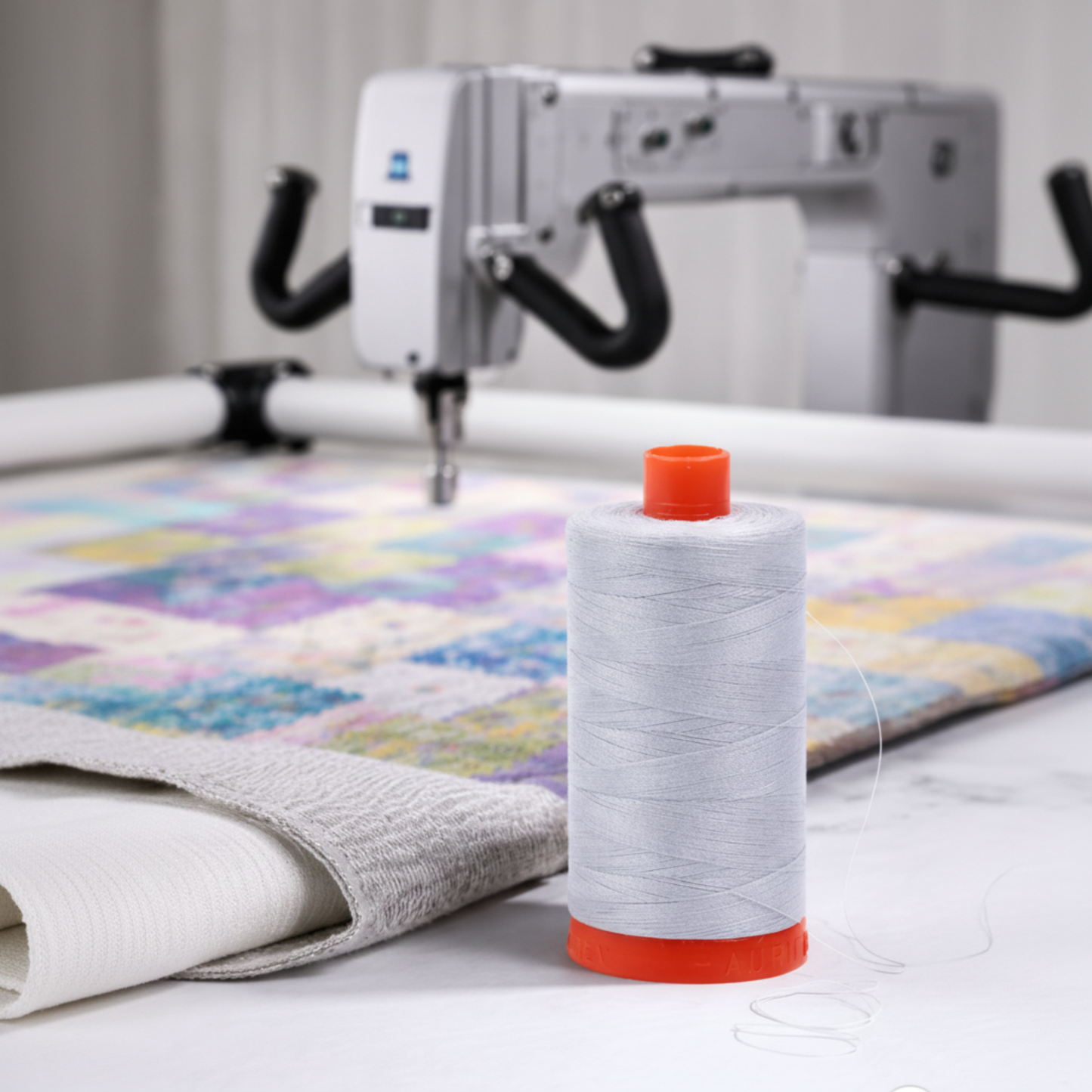 Aurifil Mako Cotton Thread 50wt Aluminum used on a longarm quilting machine over a colorful quilt.