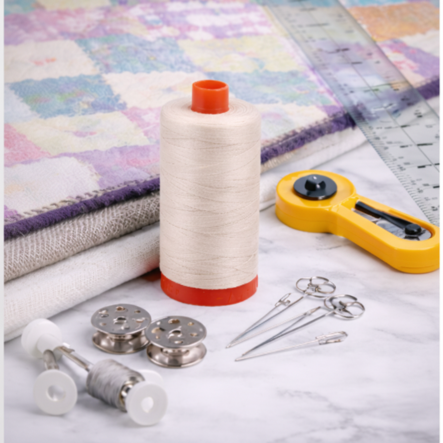 Aurifil Mako Cotton Thread 50wt Aluminum surrounded by rotary cutter, needles, and quilting tools.