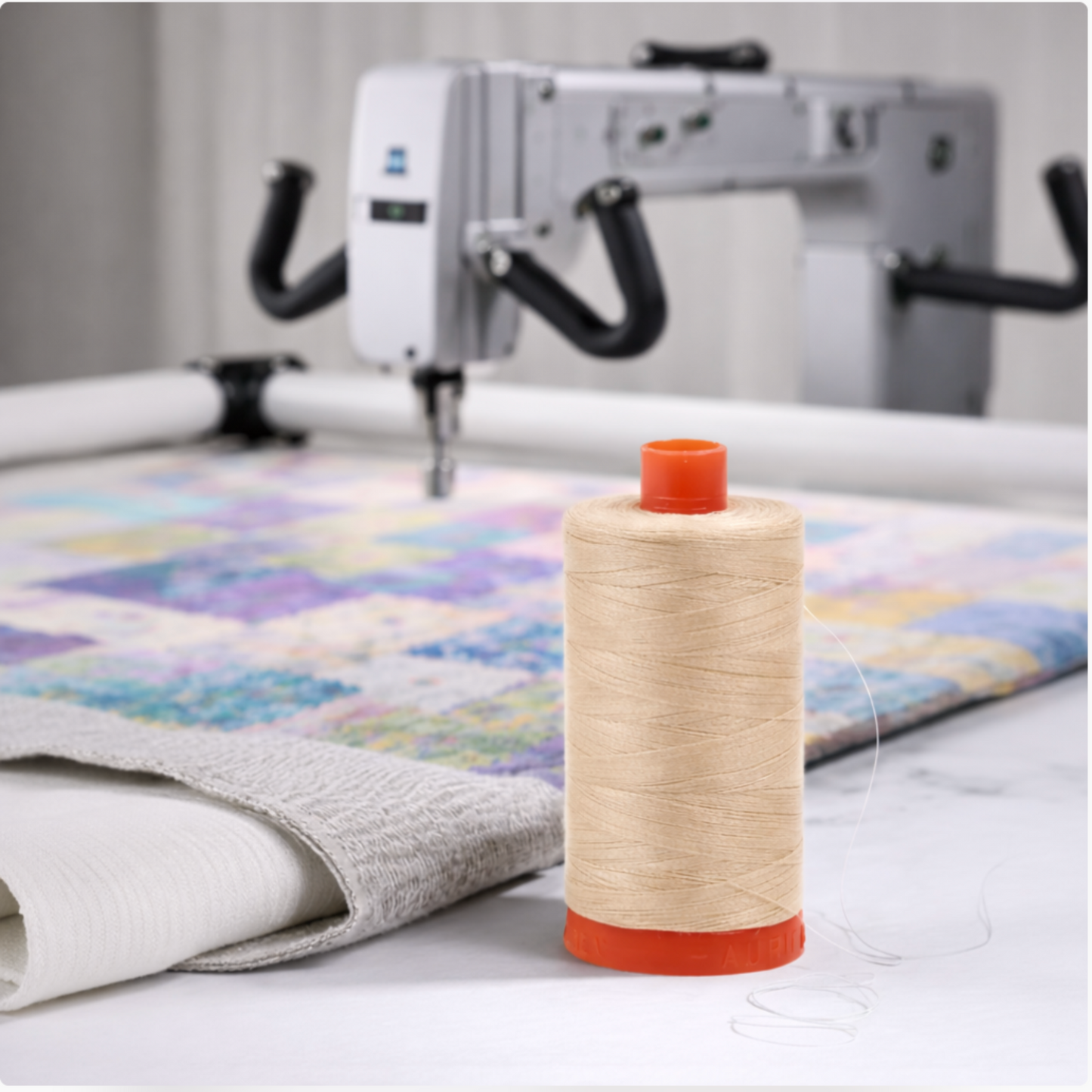 Aurifil Mako Cotton Thread 50wt Aluminum used on a longarm quilting machine over a colorful quilt.